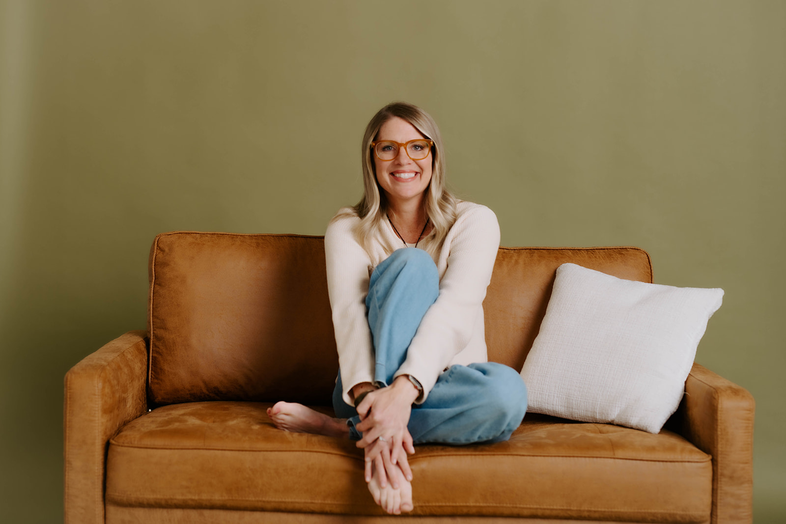 Julie Holly smiling and sitting cross-legged on a leather sofa